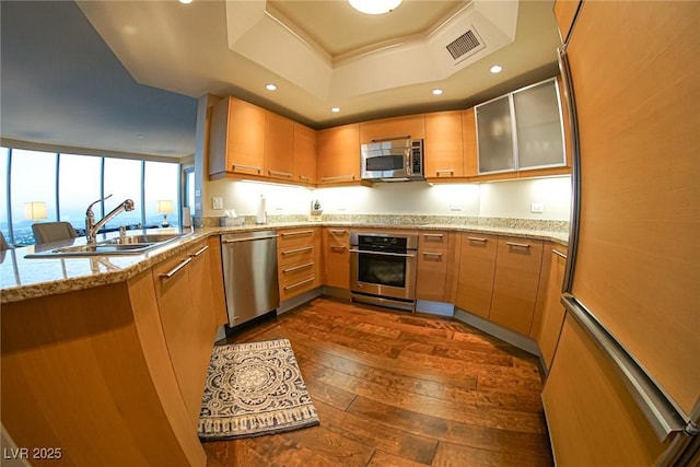 kitchen featuring visible vents, dark wood-style flooring, a tray ceiling, stainless steel appliances, and a sink