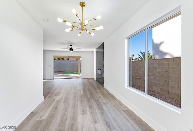 interior space featuring light wood-type flooring, a wealth of natural light, baseboards, and ceiling fan with notable chandelier