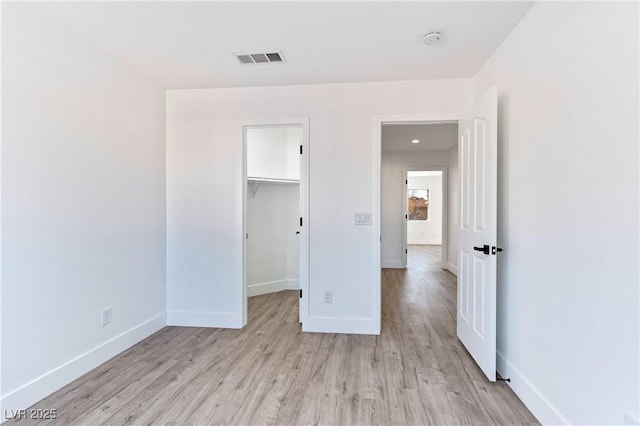 unfurnished bedroom featuring a spacious closet, light wood-style flooring, visible vents, and baseboards