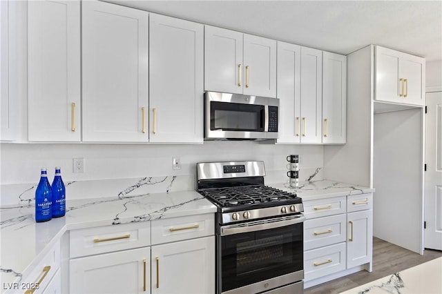 kitchen with appliances with stainless steel finishes, white cabinets, light wood-style flooring, and light stone countertops