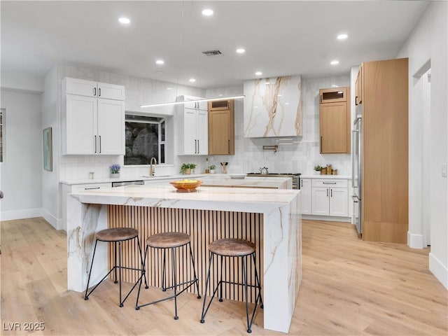 kitchen with decorative backsplash, light stone counters, a center island, light wood-style floors, and a kitchen bar