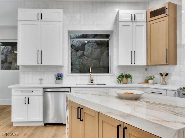 kitchen with dishwasher, backsplash, a sink, and light stone countertops