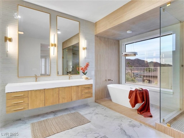 bathroom featuring double vanity, marble finish floor, a freestanding tub, and tile walls