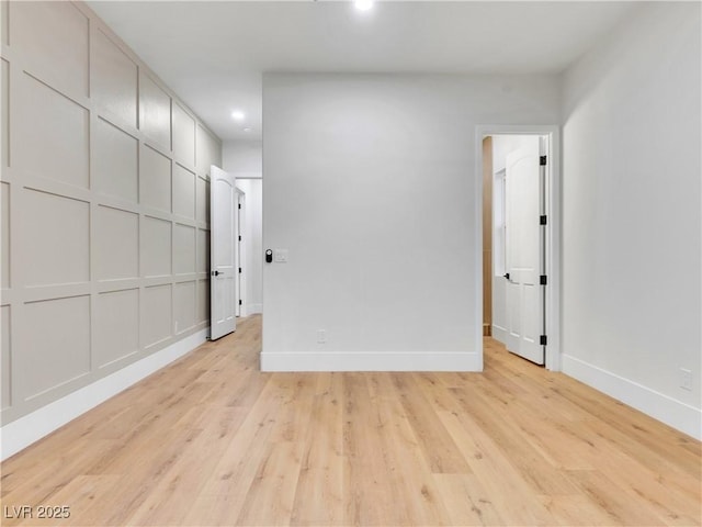 empty room featuring light wood-style floors, recessed lighting, a decorative wall, and baseboards