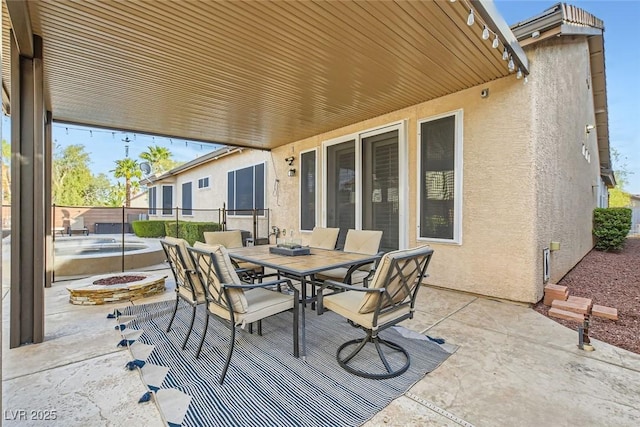 view of patio / terrace featuring an in ground hot tub, outdoor dining space, an outdoor fire pit, and fence