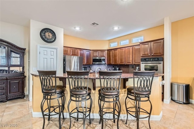 kitchen featuring tasteful backsplash, visible vents, an island with sink, stainless steel appliances, and a kitchen bar