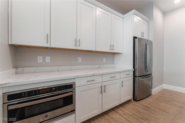 kitchen with light stone counters, stainless steel appliances, white cabinetry, baseboards, and light wood-type flooring