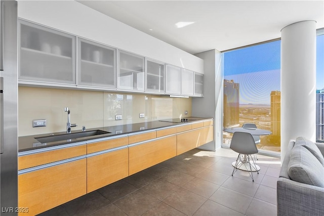 kitchen with a wall of windows, a sink, dark tile patterned floors, glass insert cabinets, and black electric cooktop