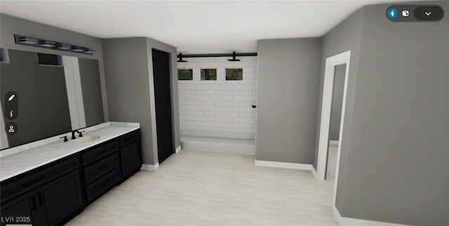 bathroom featuring baseboards, wood finished floors, tiled shower, and vanity