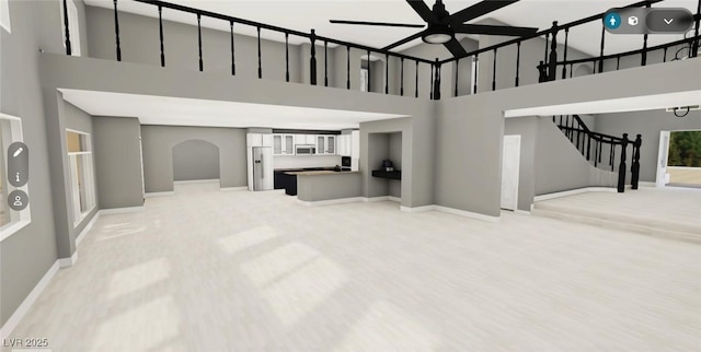 living room featuring baseboards, a towering ceiling, ceiling fan, stairway, and light wood-type flooring