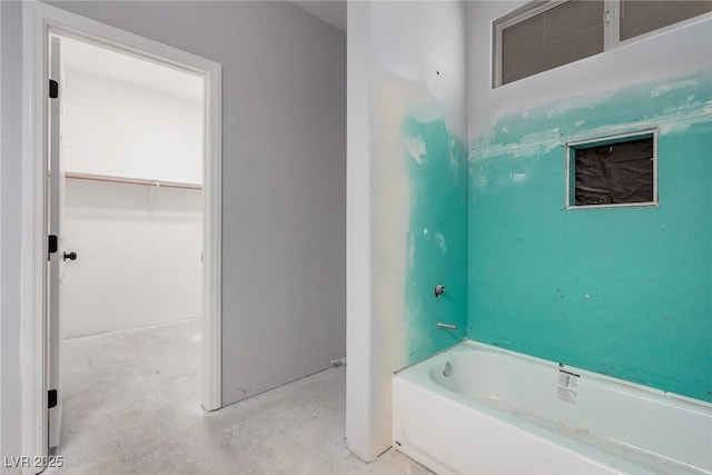 bathroom with a spacious closet, concrete floors, and a bathing tub