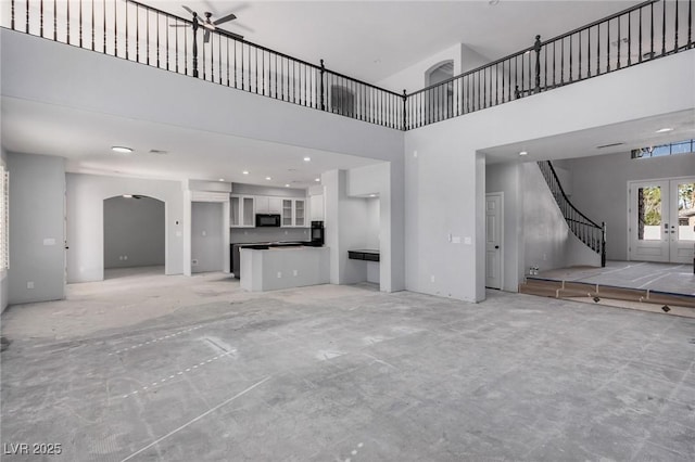 unfurnished living room with arched walkways, a high ceiling, stairs, concrete flooring, and french doors