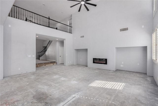 unfurnished living room featuring a glass covered fireplace, visible vents, ceiling fan, and stairway