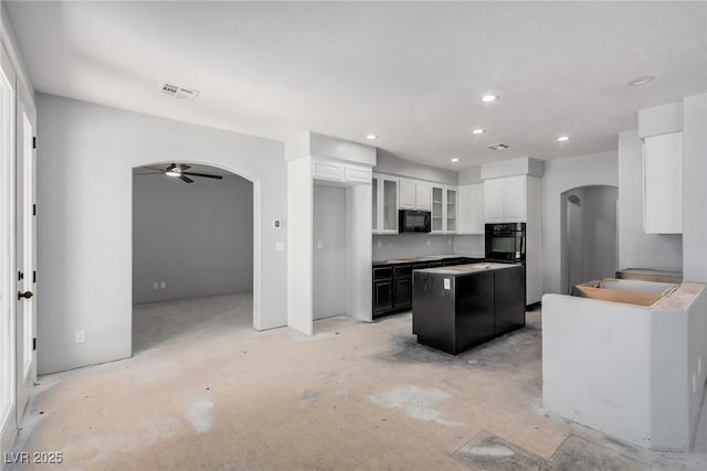 kitchen featuring visible vents, arched walkways, a center island, concrete flooring, and black appliances