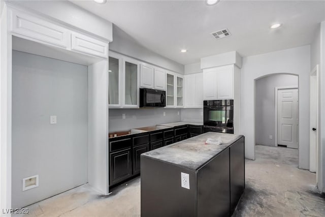 kitchen with arched walkways, visible vents, a center island, black appliances, and unfinished concrete floors