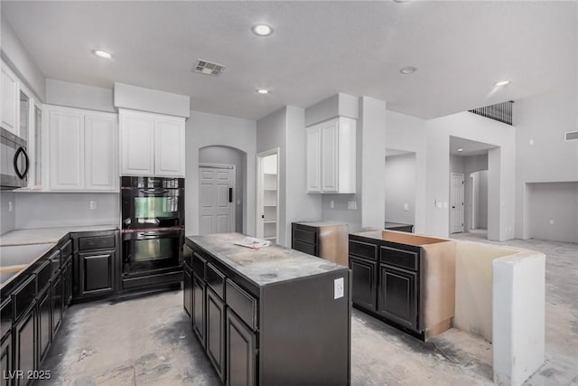 kitchen with arched walkways, visible vents, white cabinets, a kitchen island, and dark cabinets