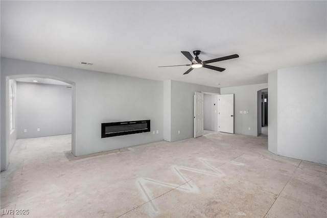 unfurnished living room with ceiling fan, arched walkways, and a glass covered fireplace