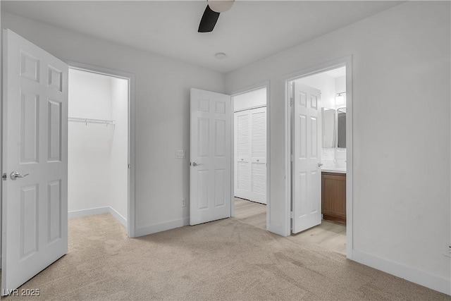 unfurnished bedroom with light carpet, baseboards, a walk in closet, and a closet