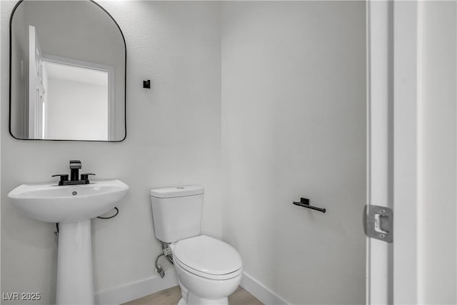 half bath featuring toilet, a sink, baseboards, and wood finished floors