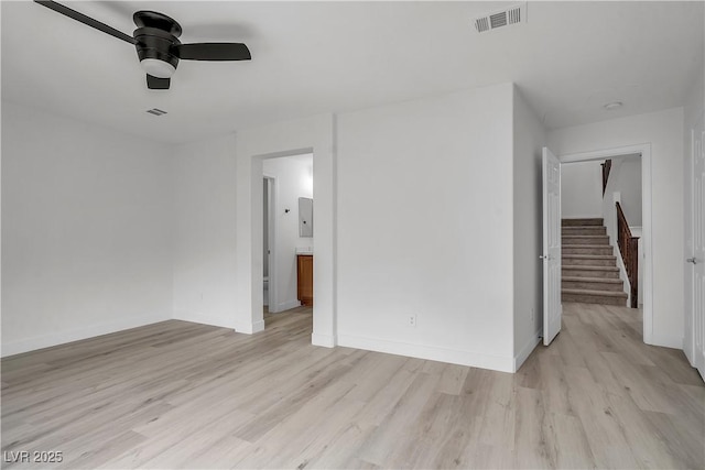 spare room with stairs, light wood finished floors, visible vents, and baseboards