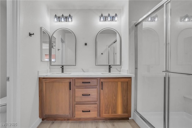 full bathroom featuring double vanity, a stall shower, a sink, and toilet