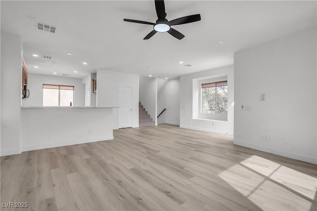 unfurnished living room with light wood-style flooring, stairway, visible vents, and a healthy amount of sunlight