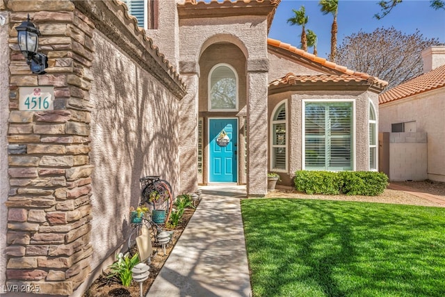 doorway to property featuring a lawn, a tile roof, and stucco siding