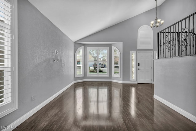 interior space with baseboards, a chandelier, a textured wall, wood finished floors, and high vaulted ceiling