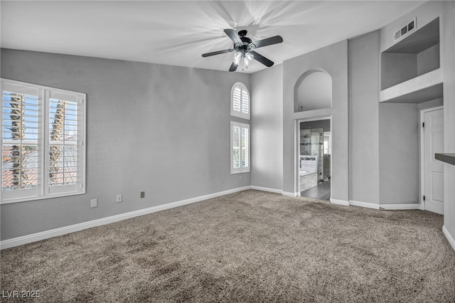 interior space with carpet floors, visible vents, a towering ceiling, ceiling fan, and baseboards