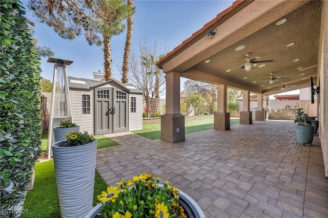 view of patio with a ceiling fan, an outbuilding, fence, and a storage unit