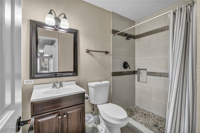 bathroom featuring toilet, a textured wall, a stall shower, and vanity