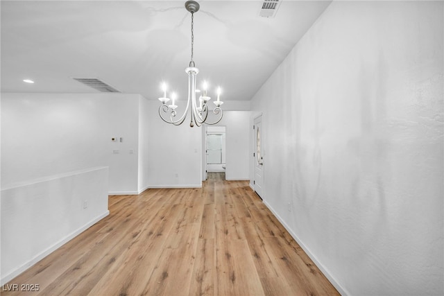 unfurnished dining area featuring visible vents, baseboards, light wood-style floors, and an inviting chandelier