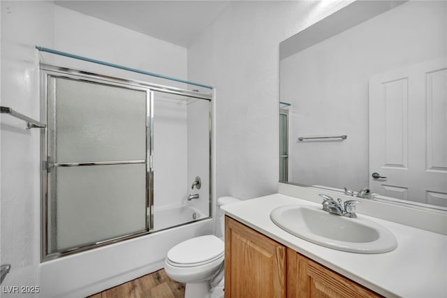 full bath with combined bath / shower with glass door, toilet, wood finished floors, and vanity