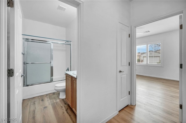 full bathroom featuring vanity, wood finished floors, visible vents, bath / shower combo with glass door, and toilet