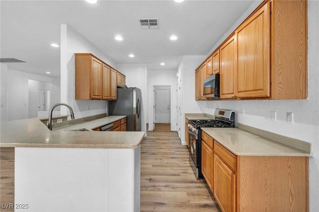 kitchen featuring visible vents, light wood finished floors, a peninsula, a sink, and appliances with stainless steel finishes