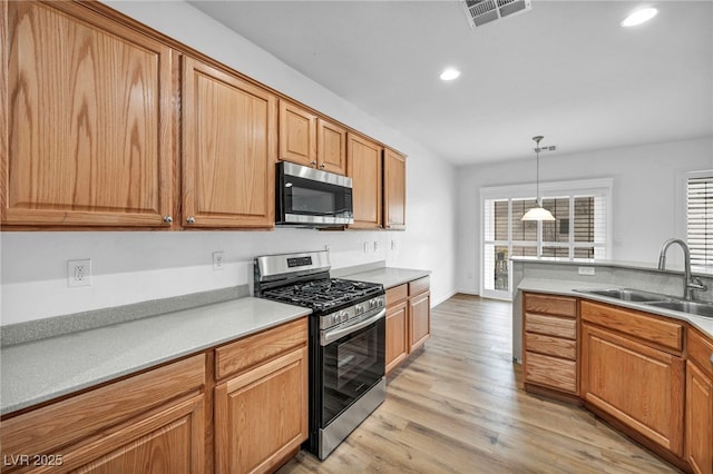 kitchen featuring visible vents, decorative light fixtures, light wood-type flooring, appliances with stainless steel finishes, and a sink