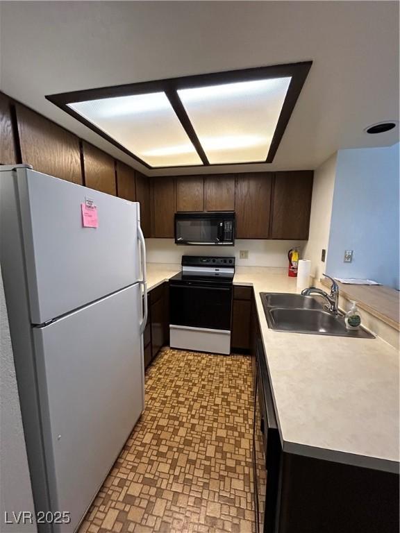 kitchen featuring dark brown cabinetry, black appliances, light countertops, and a sink