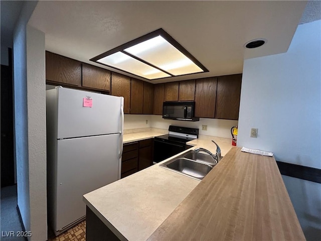 kitchen featuring black microwave, range with electric stovetop, a sink, dark brown cabinets, and freestanding refrigerator