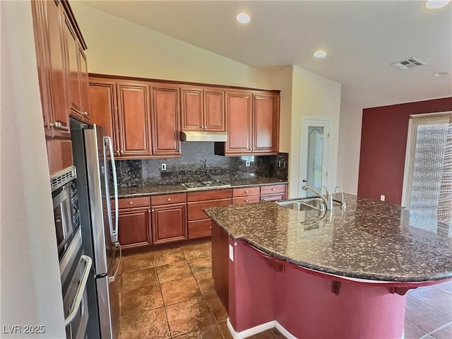 kitchen with under cabinet range hood, visible vents, a kitchen breakfast bar, appliances with stainless steel finishes, and backsplash