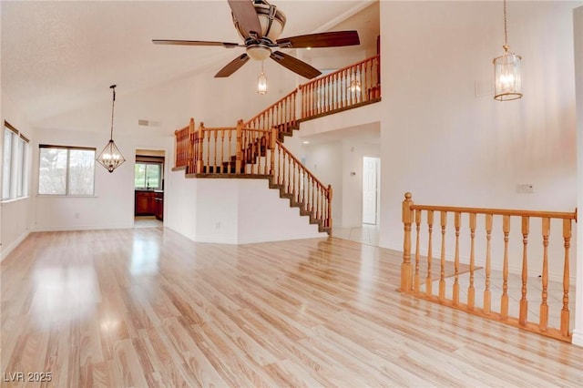 unfurnished living room featuring high vaulted ceiling, light wood-style flooring, stairway, and baseboards