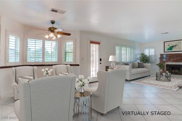 living area featuring a fireplace with raised hearth, light tile patterned floors, visible vents, and a ceiling fan