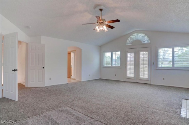 unfurnished room featuring lofted ceiling, arched walkways, a textured ceiling, and light colored carpet