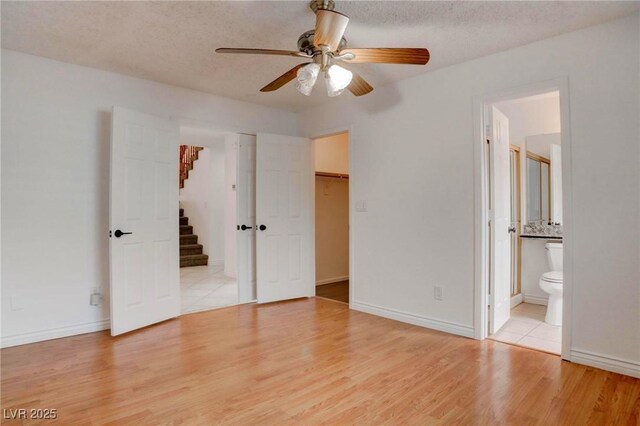 unfurnished bedroom featuring baseboards, connected bathroom, a spacious closet, a textured ceiling, and light wood-style floors