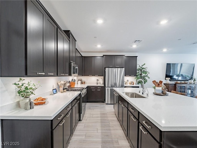 kitchen with visible vents, appliances with stainless steel finishes, a kitchen island with sink, light countertops, and a sink