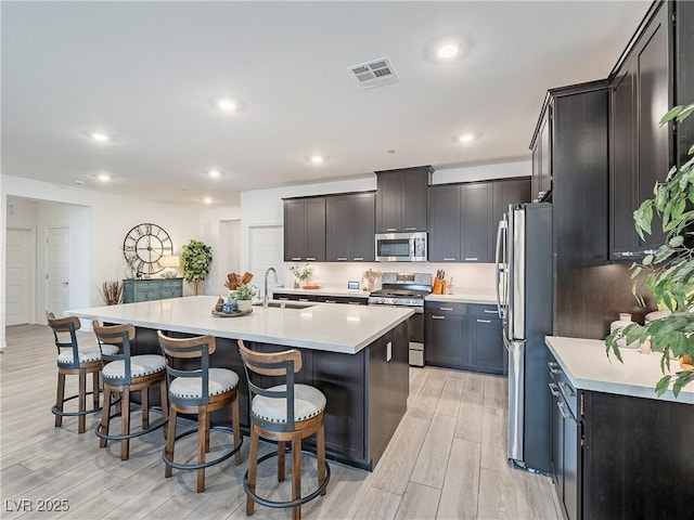 kitchen featuring visible vents, a breakfast bar area, appliances with stainless steel finishes, wood tiled floor, and a sink