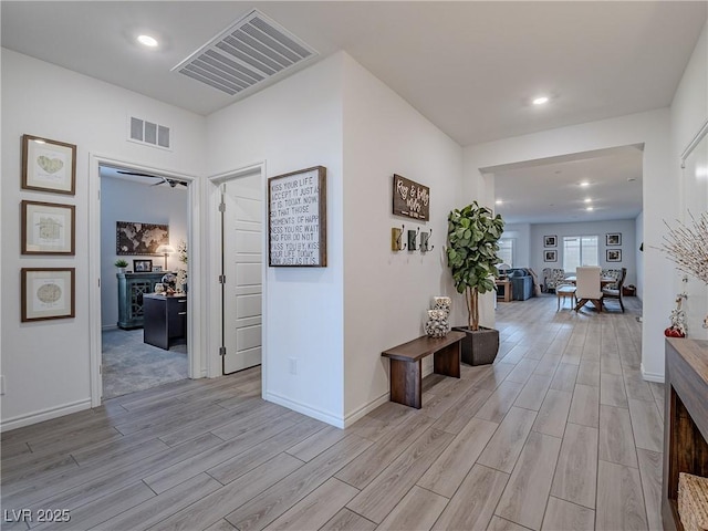 hallway featuring light wood-style floors, baseboards, and visible vents