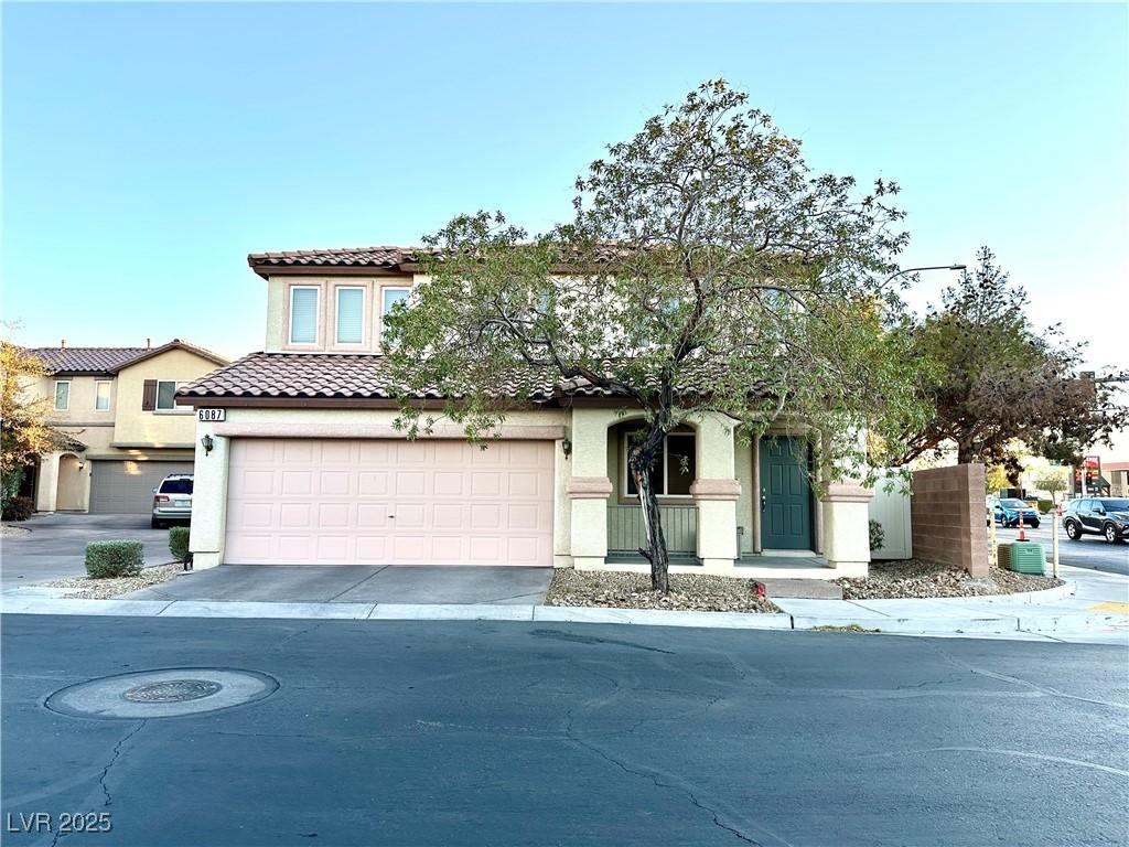 mediterranean / spanish house with a garage, a tiled roof, concrete driveway, and stucco siding