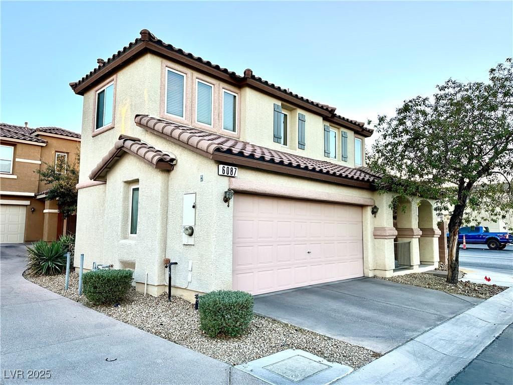 view of front of house with a garage, driveway, a tiled roof, and stucco siding