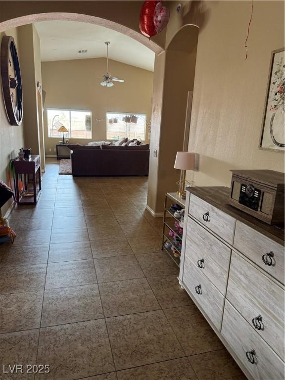 hallway featuring baseboards, arched walkways, dark tile patterned flooring, and vaulted ceiling