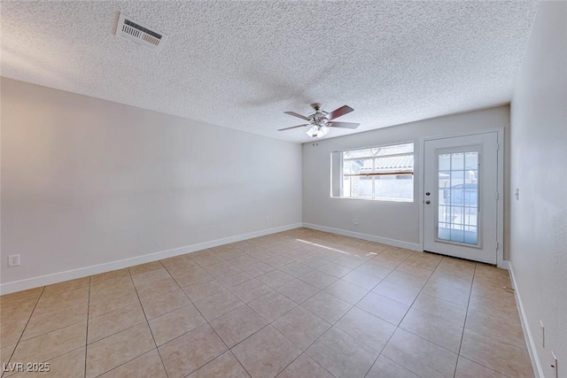 empty room featuring ceiling fan, a textured ceiling, light tile patterned flooring, visible vents, and baseboards